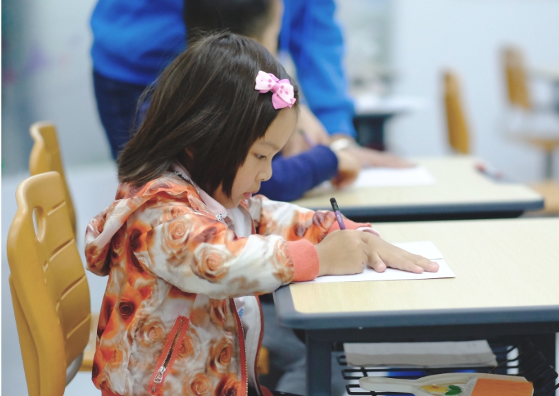 A toddler girl student writing something on her notepad