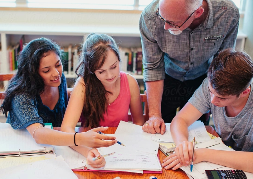 three students consulting course material together with an elder